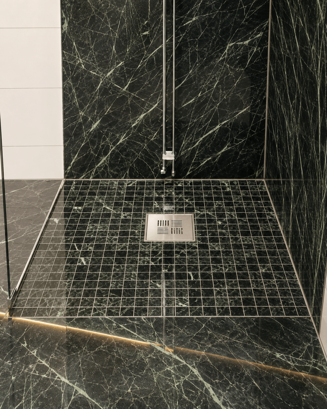 Mosaikklinker i duschgolv med golvbrunn och marmorkakel på väggarna