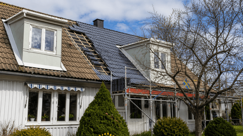 Vitt hus med pågående takbyte från äldre tegel till nytt mörkt tak