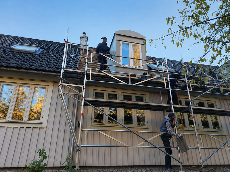 Takläggare arbetar på ställning vid nylagt svart tak