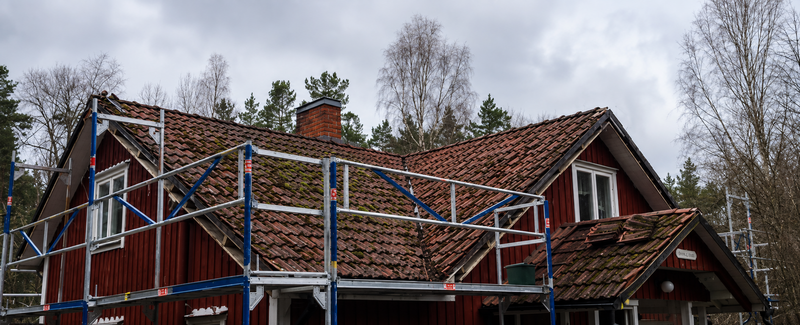 Äldre mossbevuxet tegeltak under renovering med ställning