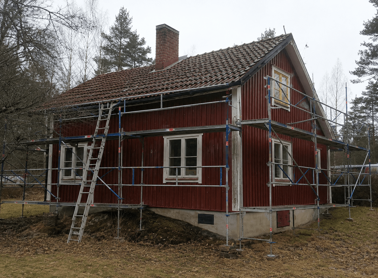 Rött trähus med ställning under renovering av tak och fasad