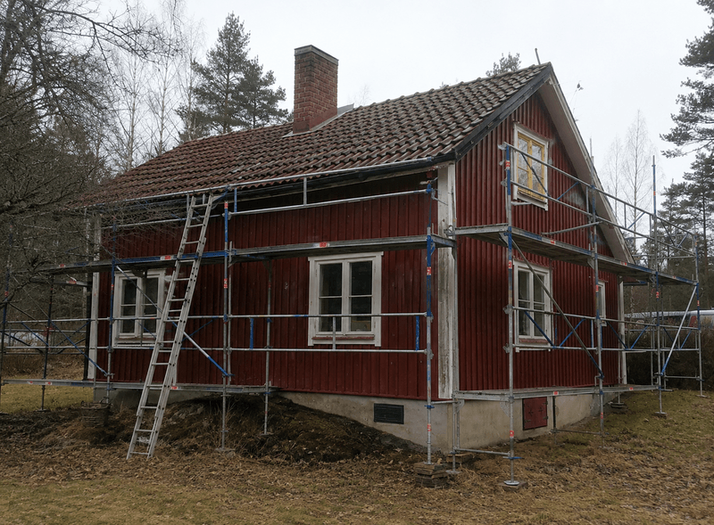 Rött trähus med ställning under renovering av tak och fasad