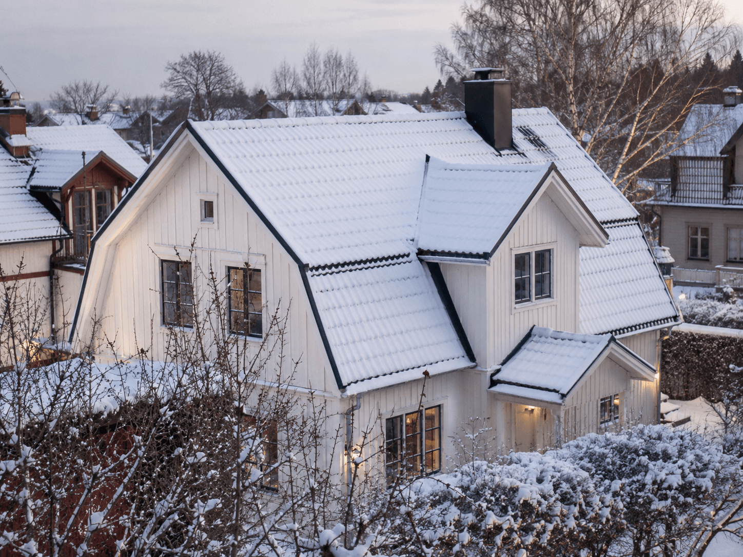 Vitt hus med snötäckt tak vintertid i skymning