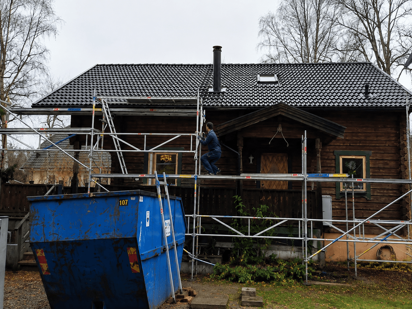Timmerhus med ställning och container inför tak- och fasadrenovering