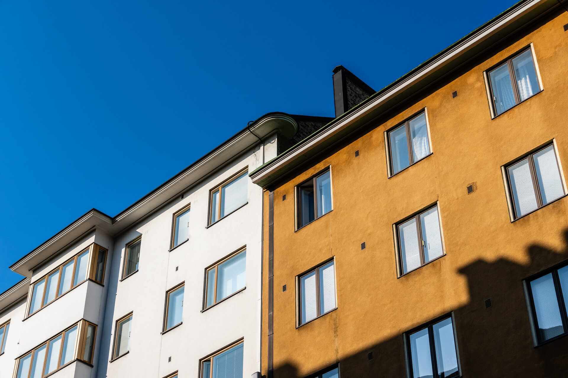 Putsade fasader i vitt och gult på flerbostadshus mot blå himmel