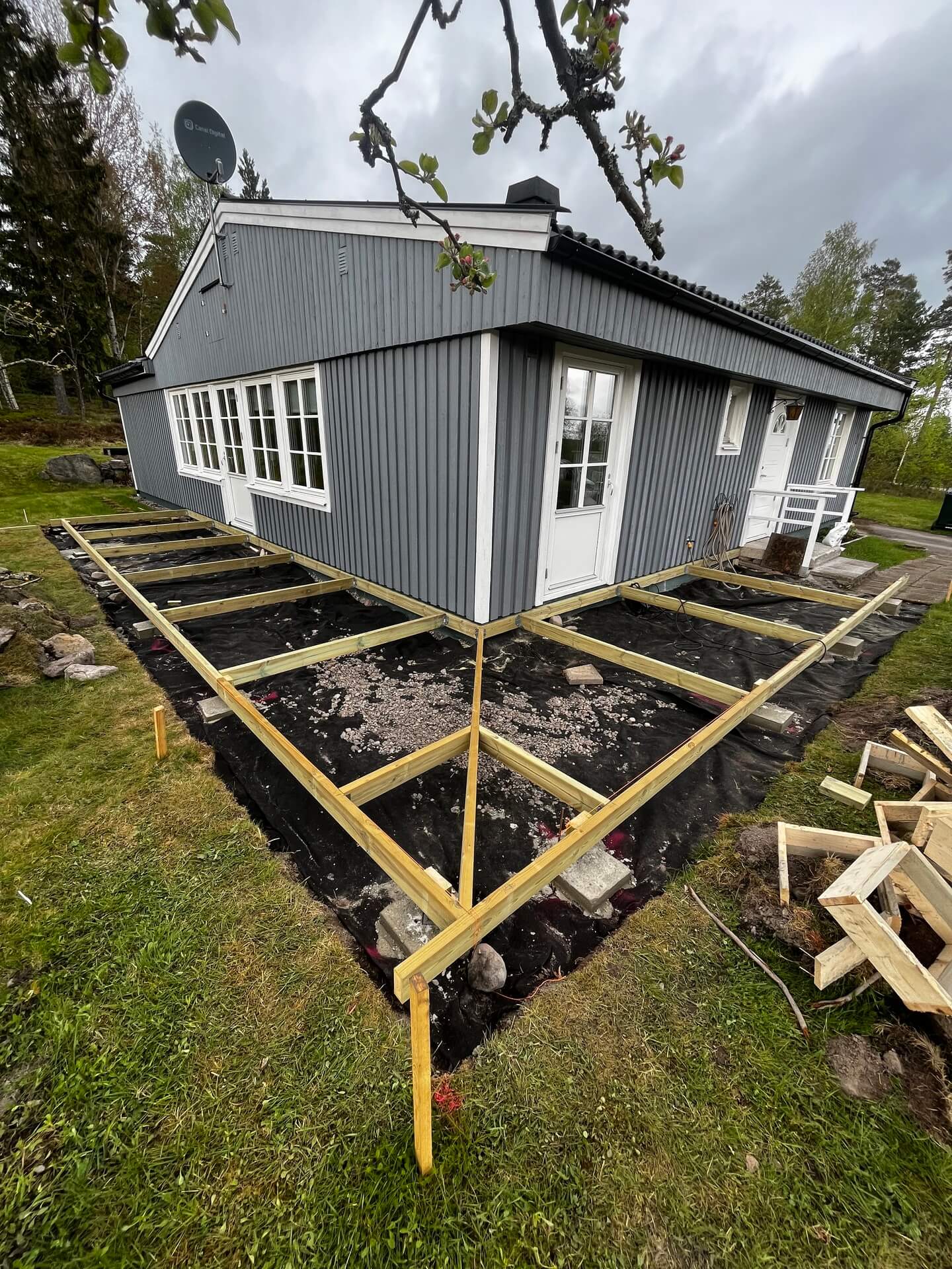 Grundläggning i trä för uteplats utanför blåmålat hus