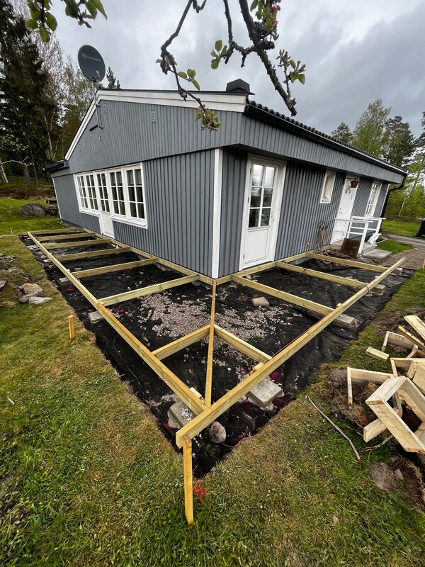 Grundläggning i trä för uteplats utanför blåmålat hus
