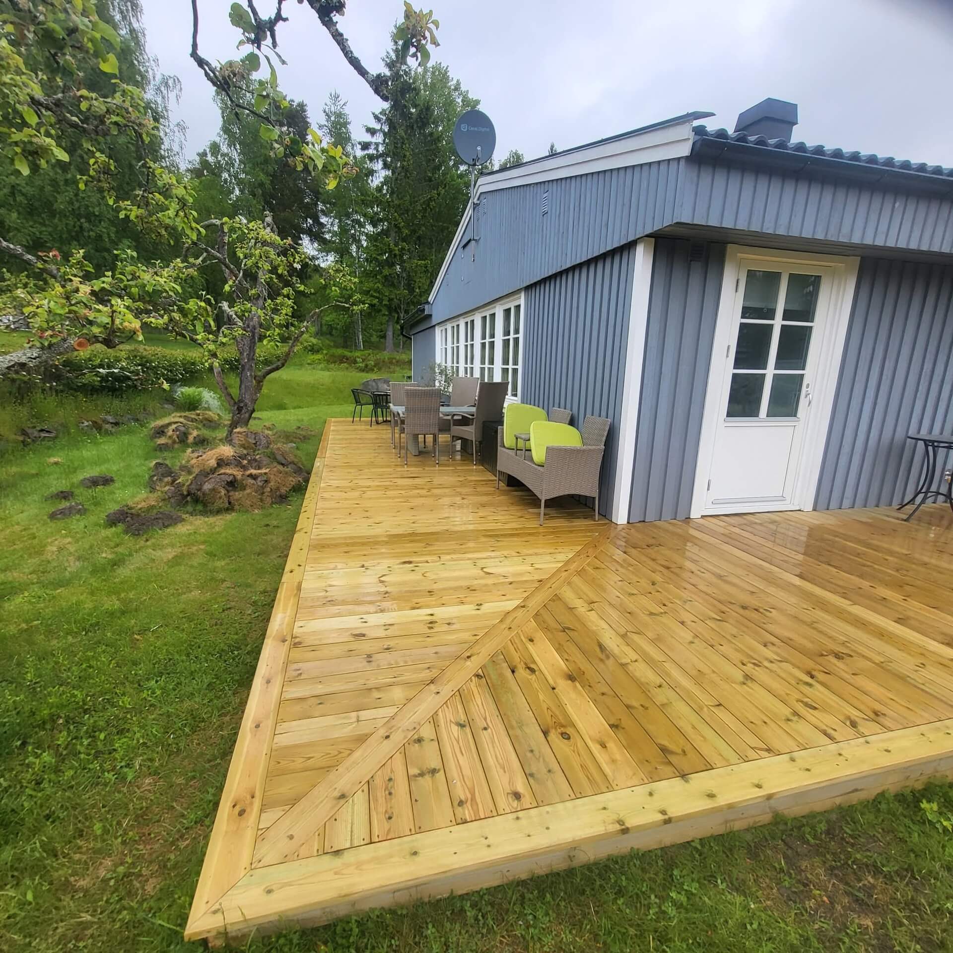 Färdig uteplats i trä med möbler utanför blåmålat hus