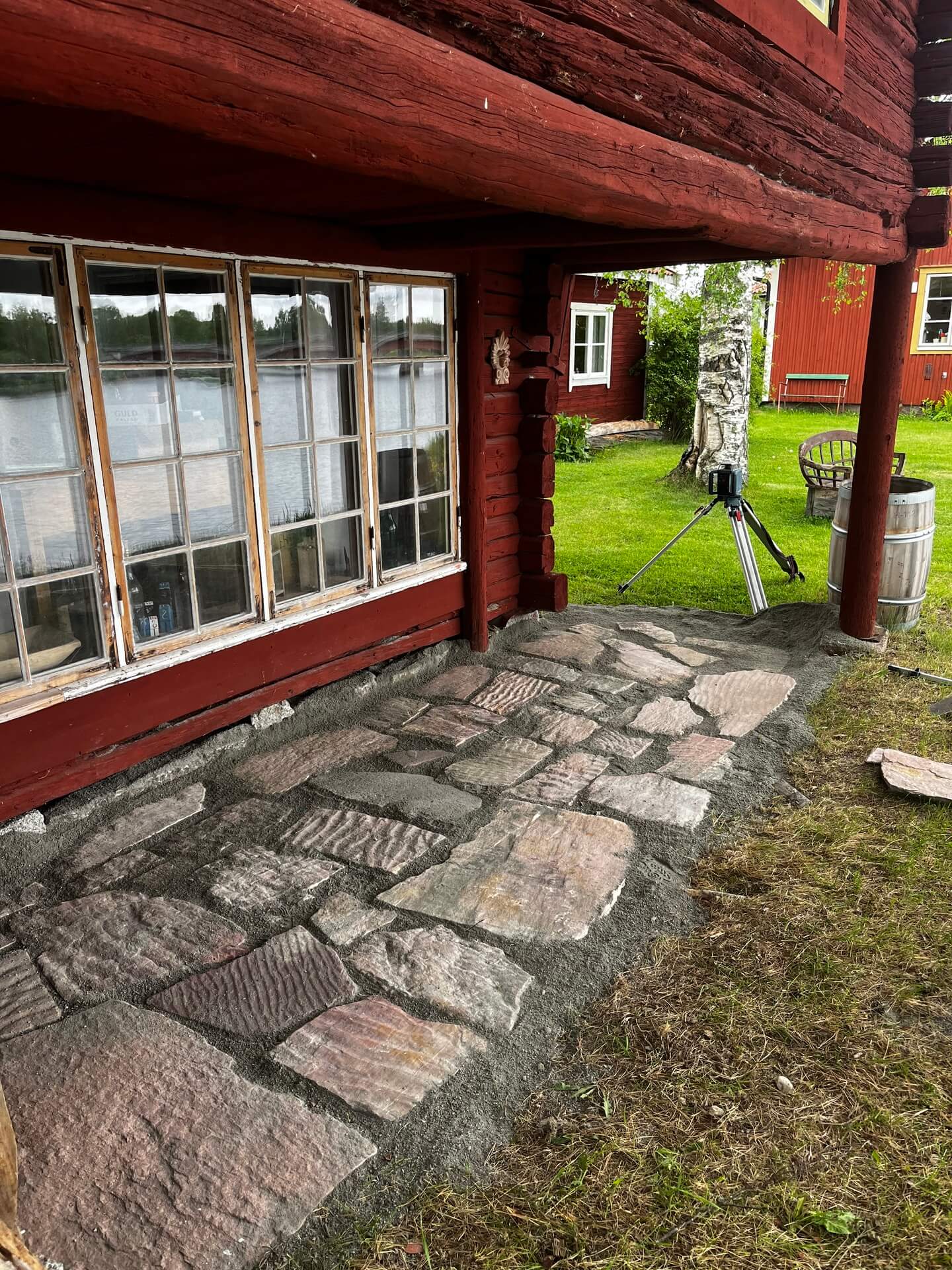 Stenlagd uteplats vid rött hus med fönsterparti under renovering