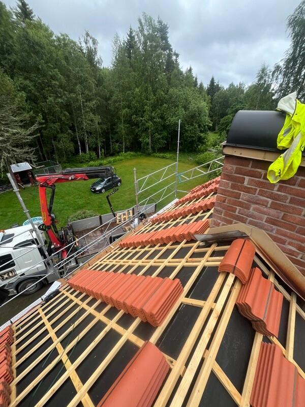 Nyläggning av rött tegeltak med skorsten och kranbil på gården