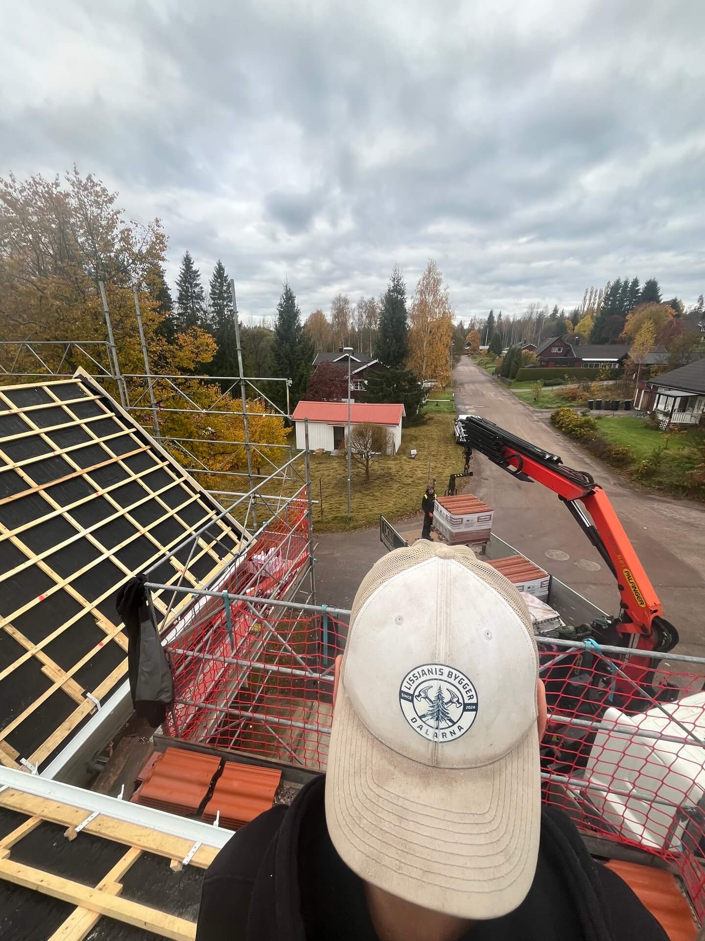 Vy över takläkt och byggarbetsplats med kranbil, hjälm i förgrunden