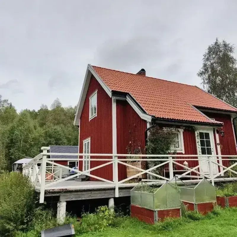Röd villa med orange tegelpannor och vit altan sedd från trädgården