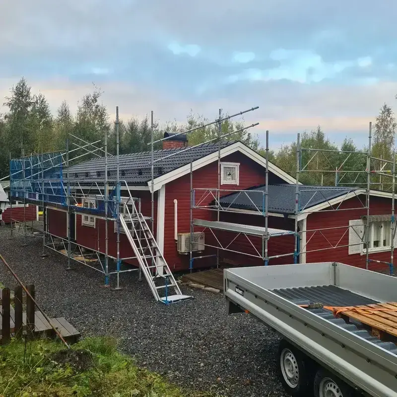 Röd villa med nylagt mörkgrått betongpannetak och byggnadsställning längs fasaden i skymning