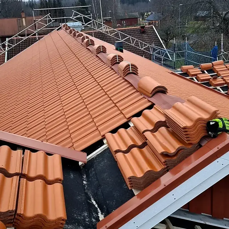 Närbild på takläggare som lägger orange tegelpannor längs takfoten med ventilationspannor längs nocken
