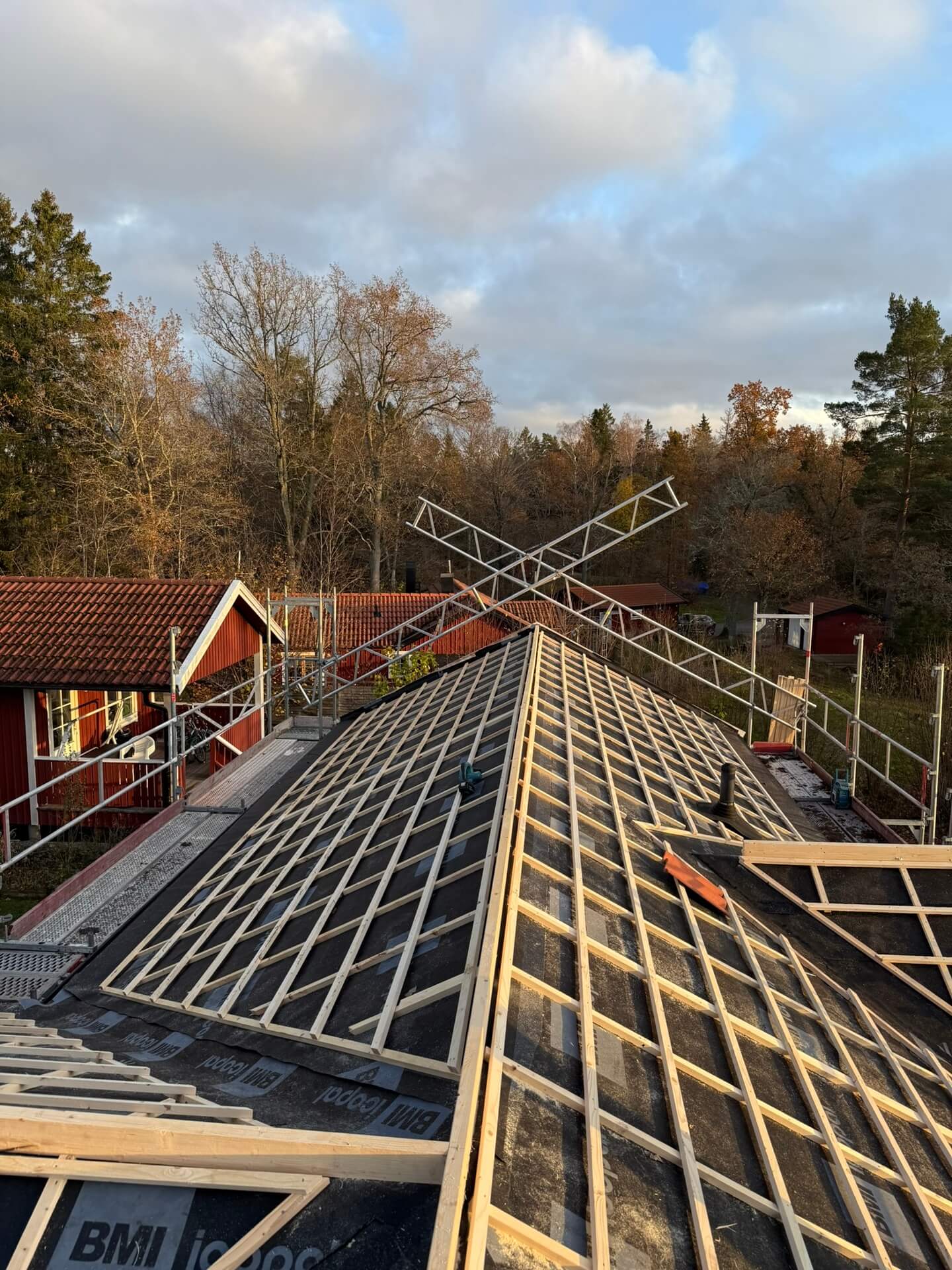 Öppen råspont på tak under pågående takbyte, med byggnadsställning och omgivande natur