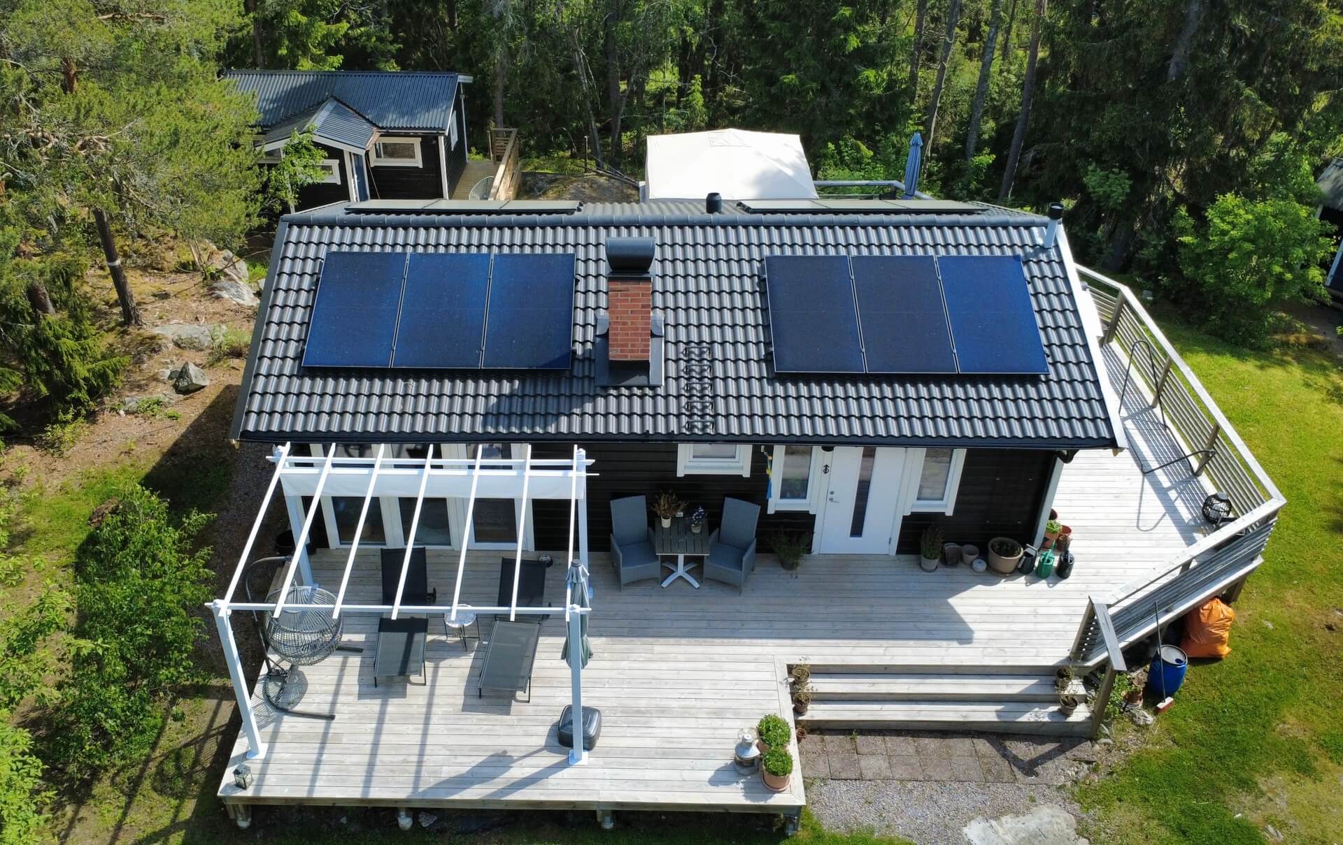 Flygbild över hus med svart tegeltak, solpaneler och uteplats
