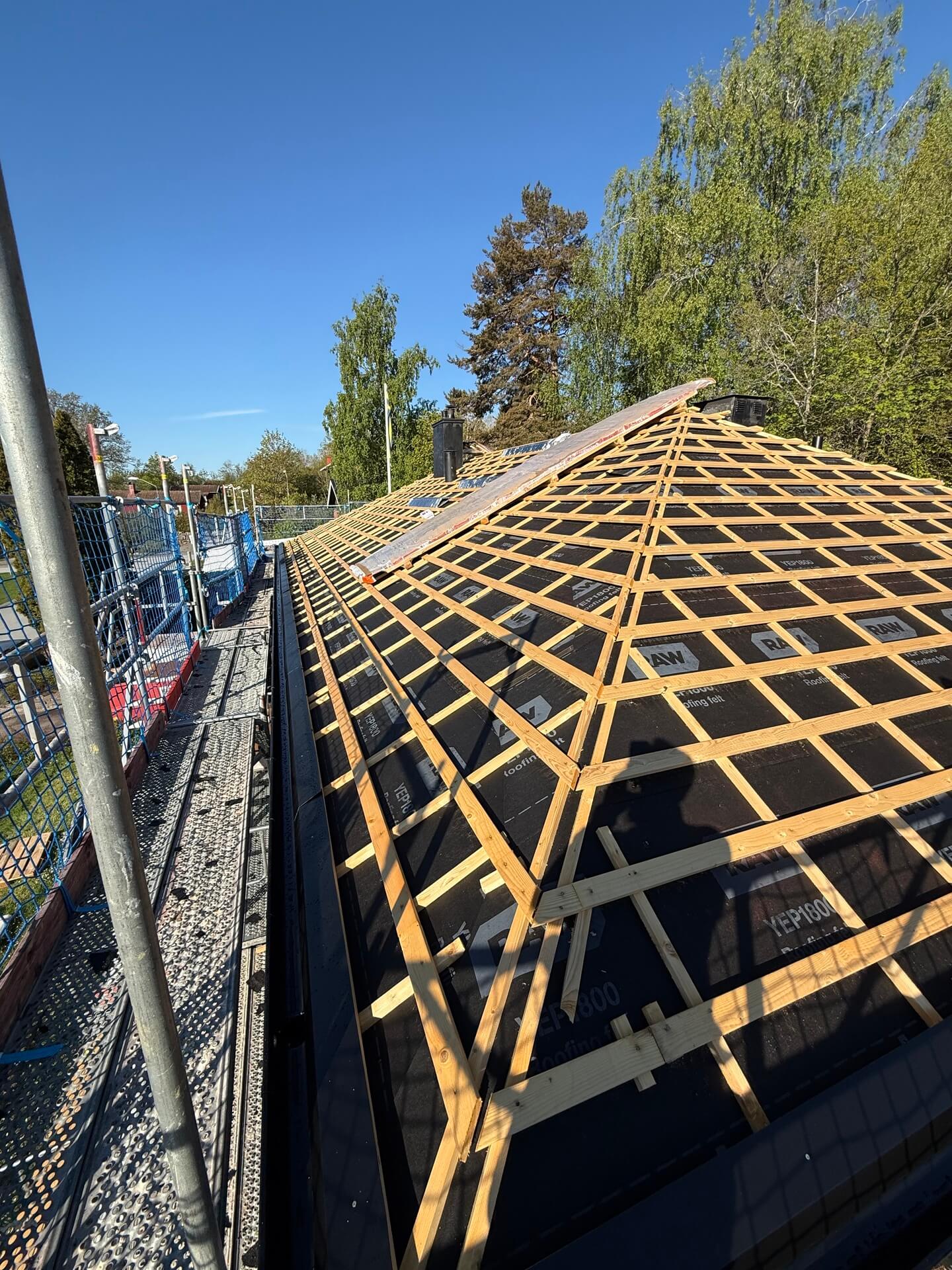 Tak under montage med läkt lagd på underlagspapp, byggnadsställning i bakgrunden
