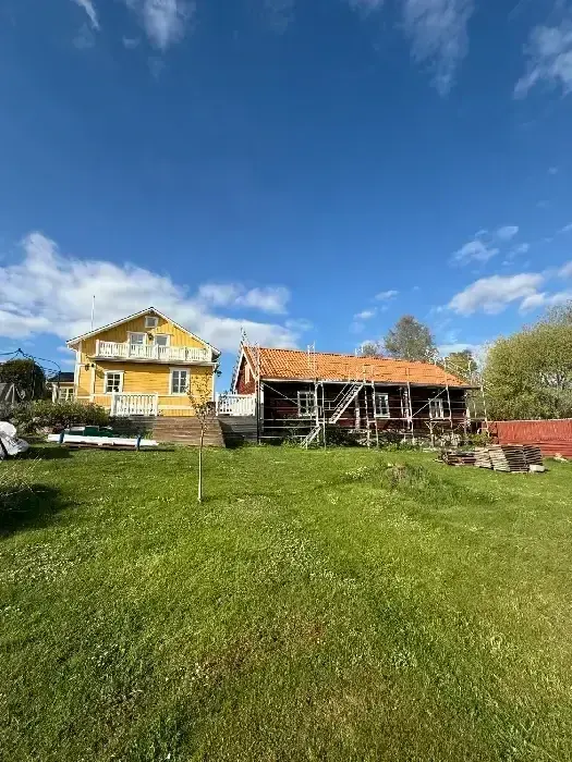 Gul villa intill rödmålad byggnad med byggnadsställning under pågående takarbete