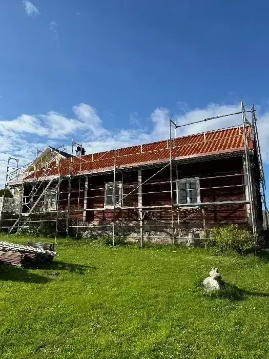 Äldre timmerhus med byggnadsställning och nylagt tegeltak under renovering