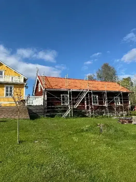 Gul och röd villa med byggnadsställning och nylagt orange tegeltak