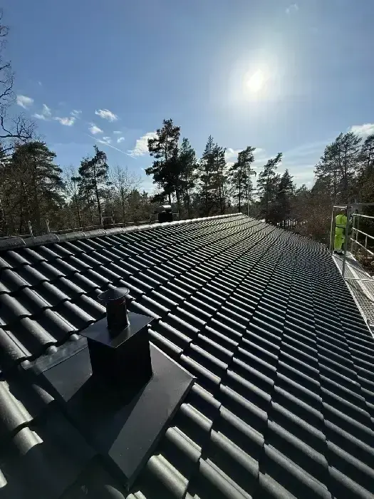 Nylagt mörkt tegeltak med ventilationshuv, montör synlig i bakgrunden