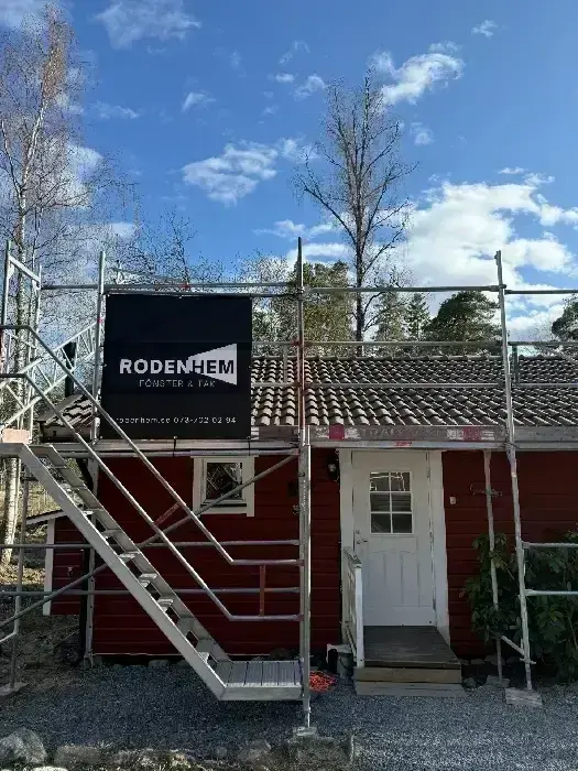 Rodenhems skylt monterad på byggnadsställning vid rödmålat hus