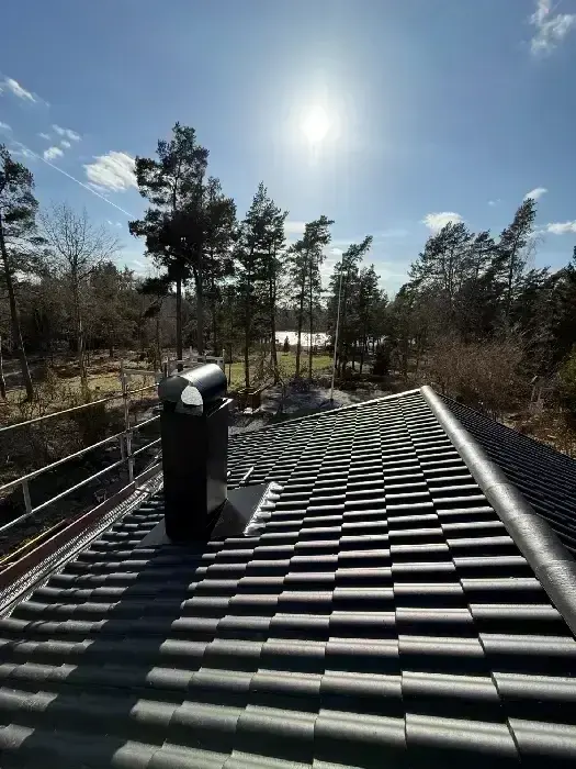 Nylagt svart tegeltak med plåtgenomföring och utsikt över skog och vatten