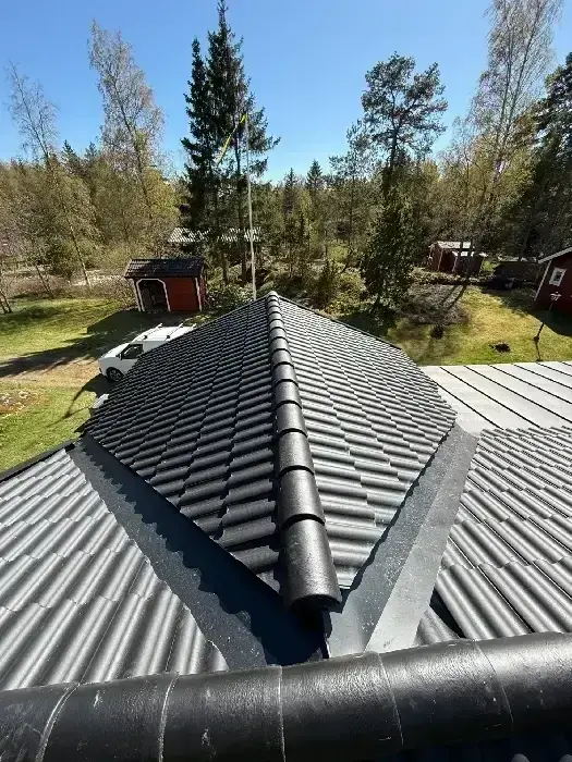 Nylagt grått tegeltak sett från nocken, med utsikt över trädgård och uthus