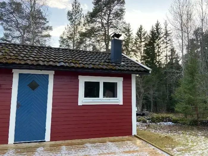 Rödmålad stuga med nylagt svart tegeltak och blå ytterdörr