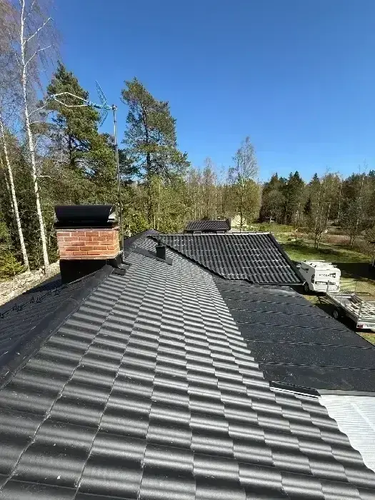 Tak under montage med svarta tegelpannor och tegelskorsten, delvis kvarvarande underlagspapp synlig