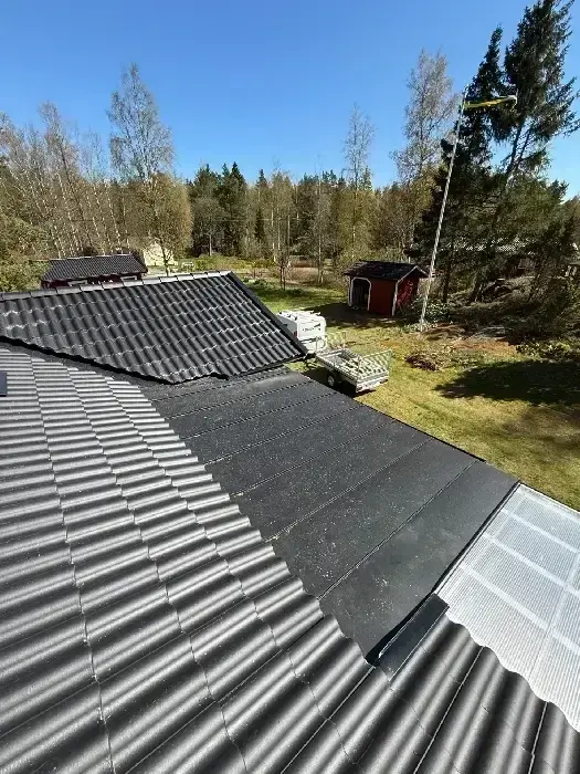 Flygbild över nylagt grått tegeltak, med uthus och skog i bakgrunden