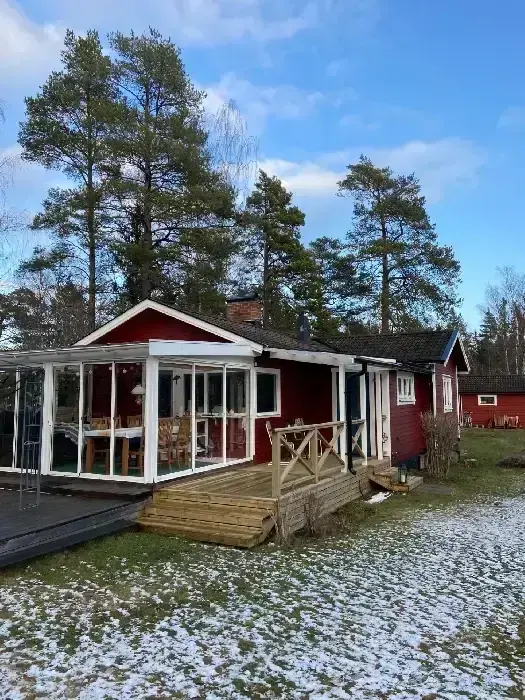 Rödmålad villa med inglasat uterum och altan, omgiven av skog