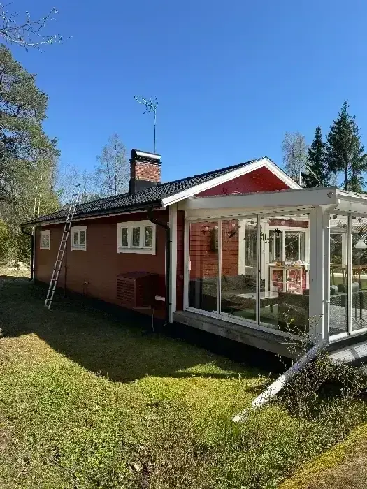 Rödmålad villa med inglasat uterum, skorsten och nylagt svart tegeltak