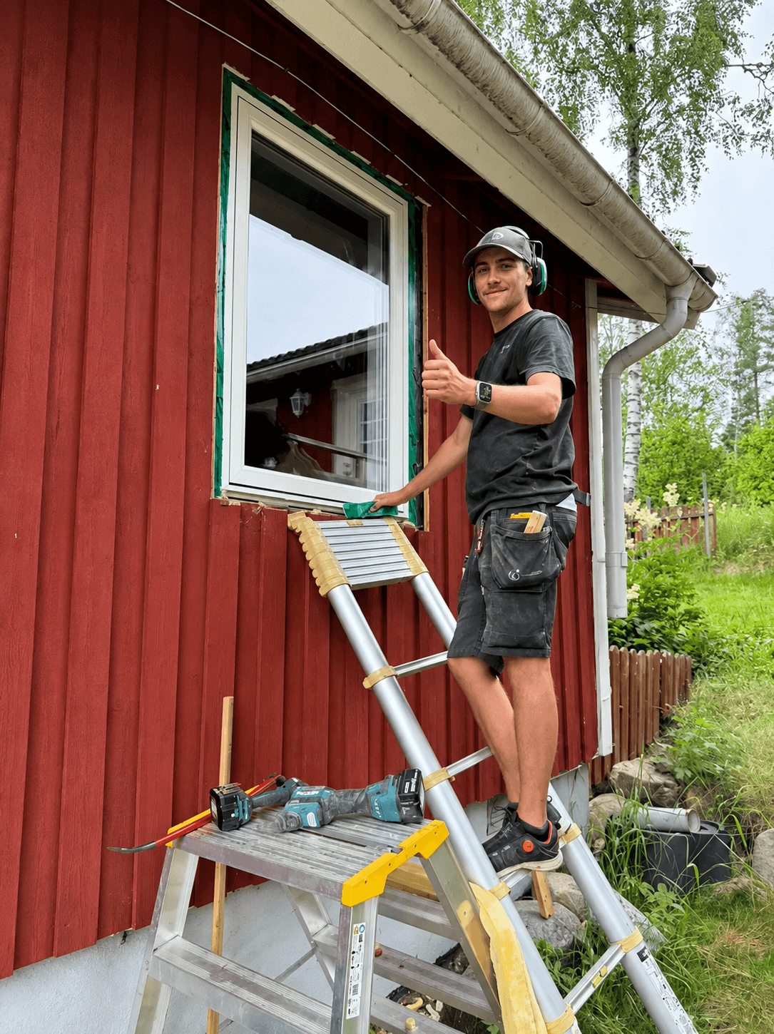 Montör som installerar nytt fönster på rödmålad husfasad, stående på stege
