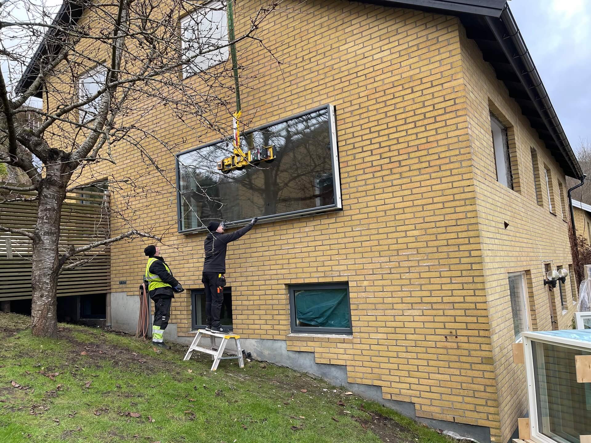 Montörer installerar stort fönsterparti med kranbil på gult tegelhus