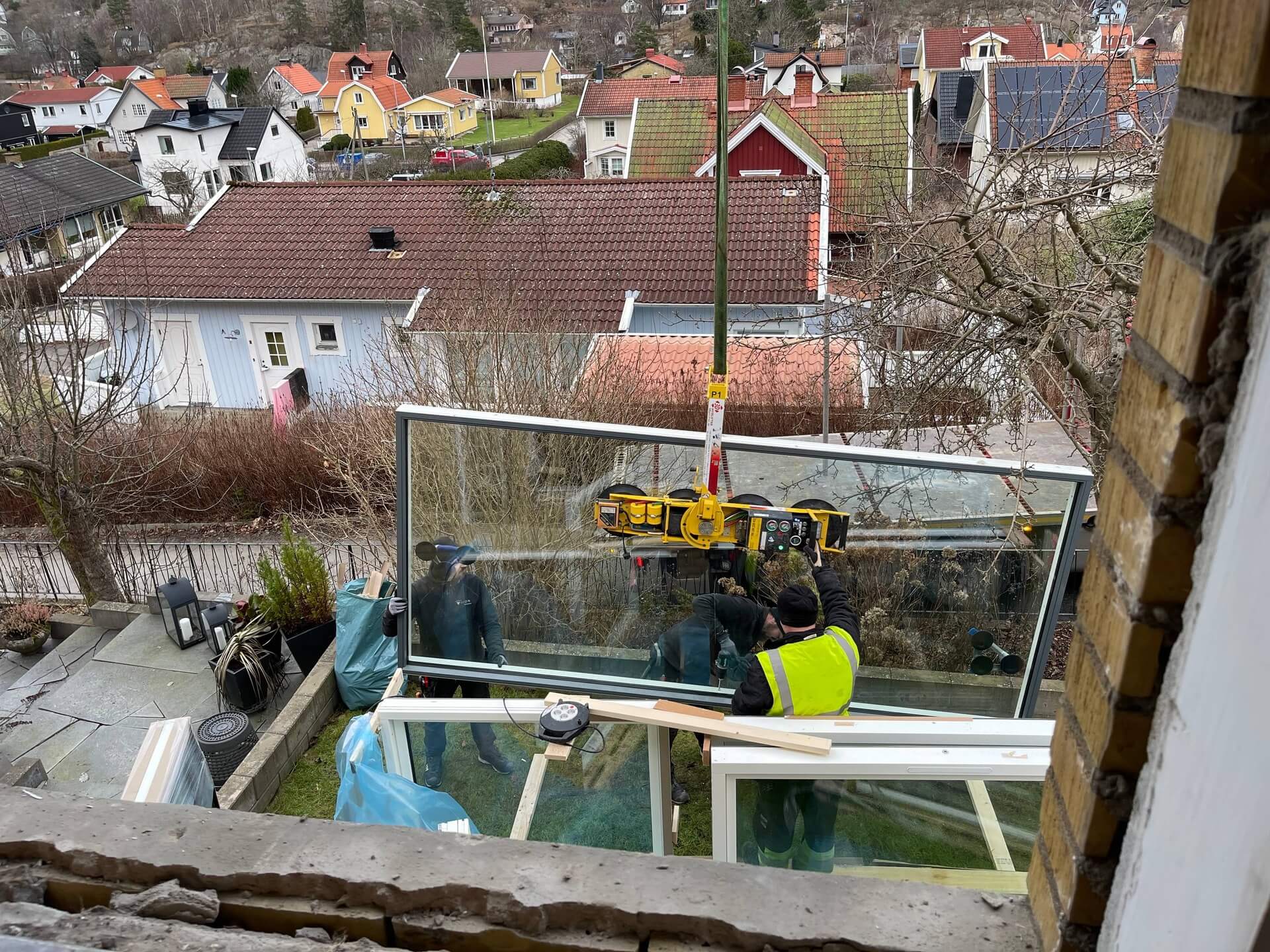 Montörer installerar stort glasparti på balkong med utsikt över villaområde