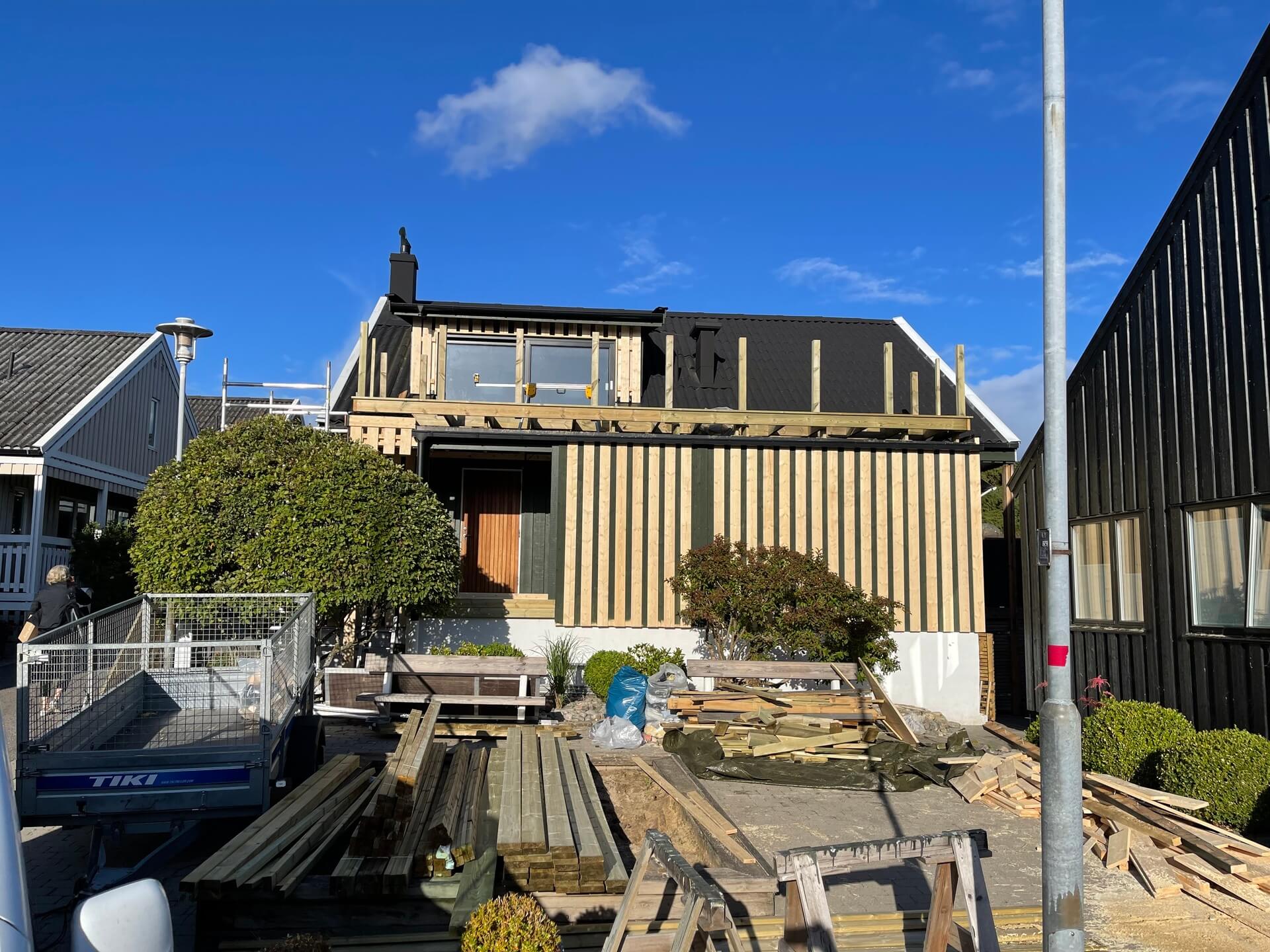 Villa under byggnation med ny träpanelfasad och altandäck under uppbyggnad