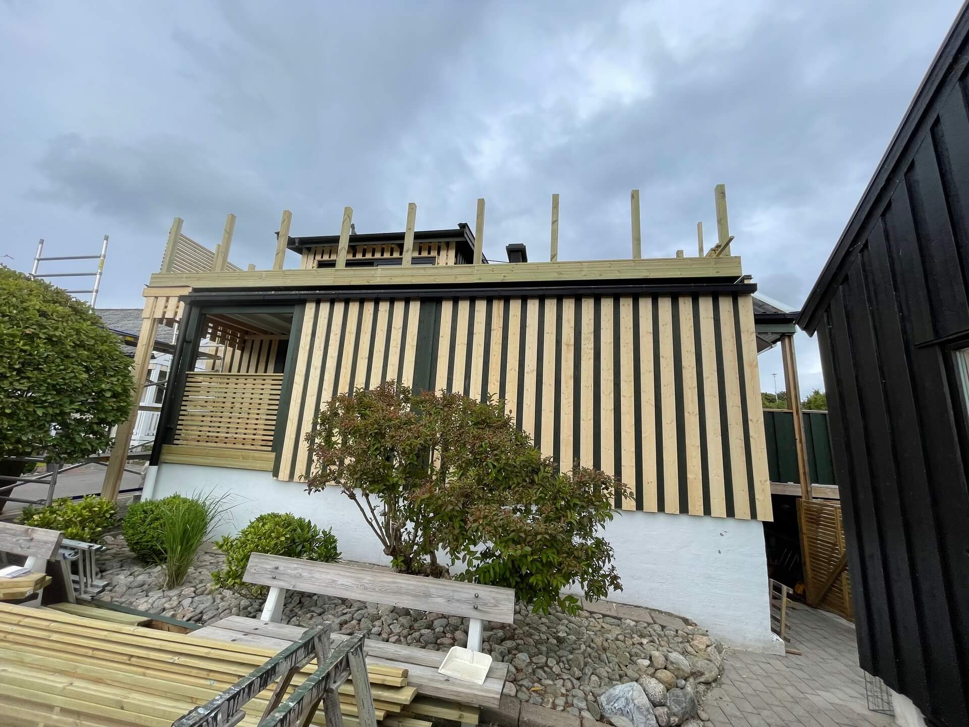 Villa med ny vertikal träpanelfasad och altankonstruktion under byggnation