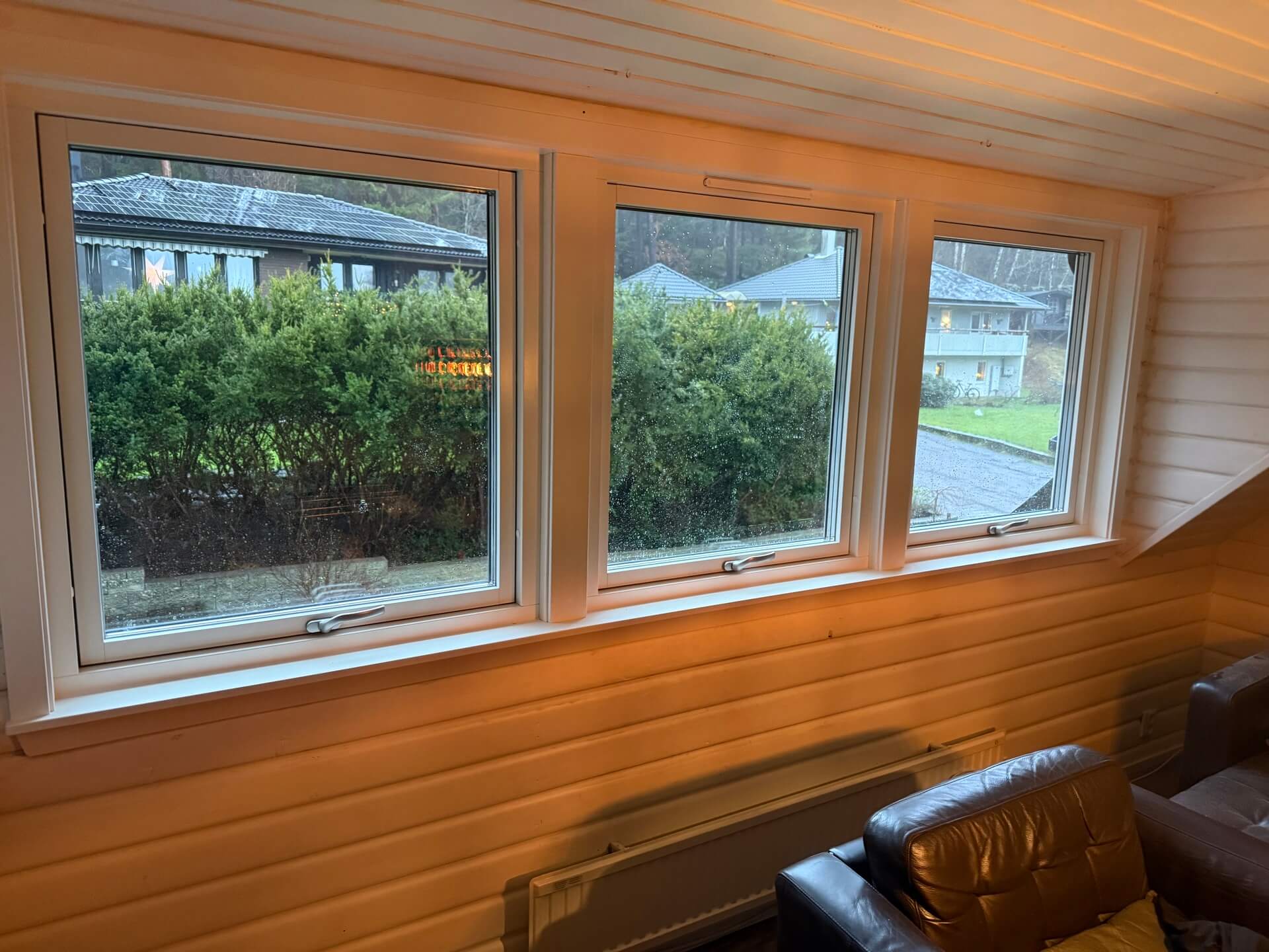 Närbild på tre vridfönster med vit karm och utsikt mot trädgård