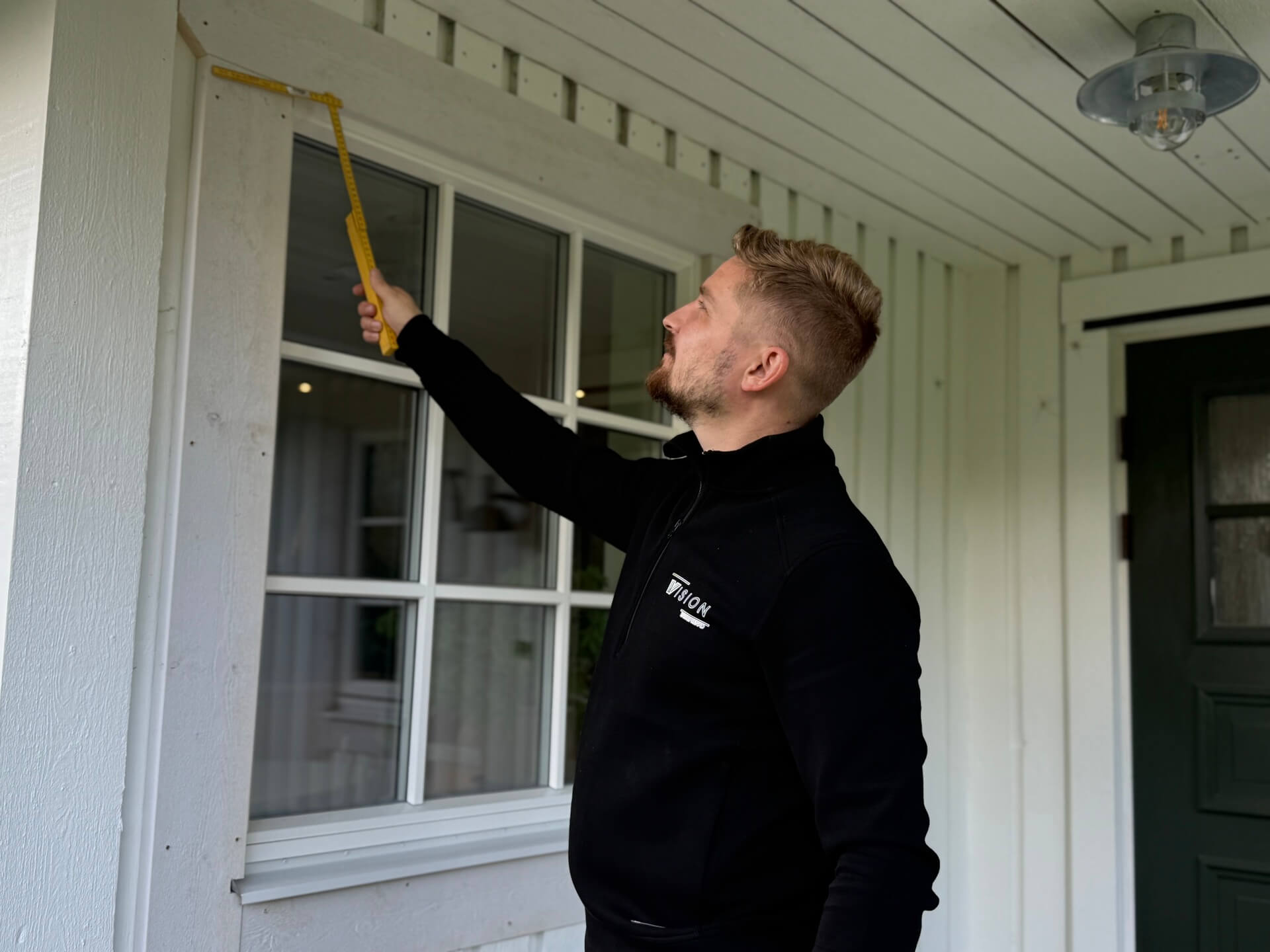 Montör applicerar tätning runt nyinstallerat spröjsat fönster på vit fasad