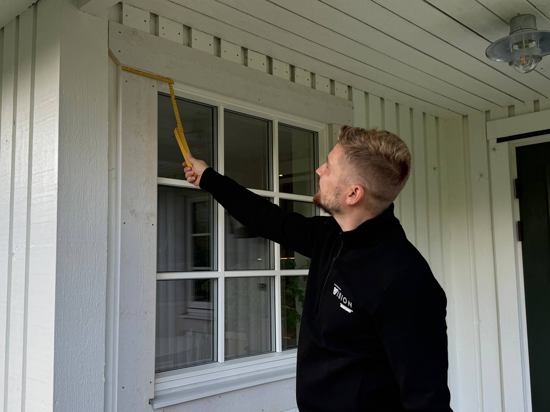 Montör från Vision Entreprenad tätar fönsterkarm utvändigt på vit träpanelfasad