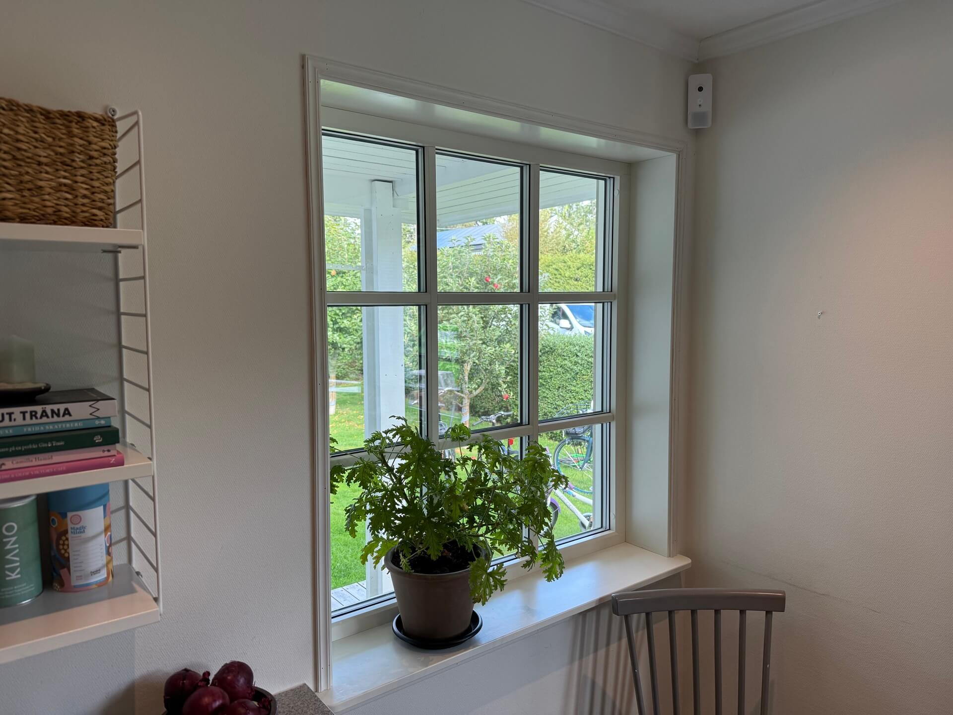 Nyinstallerat spröjsat fönster med vit karm och bred fönsterbänk i kök