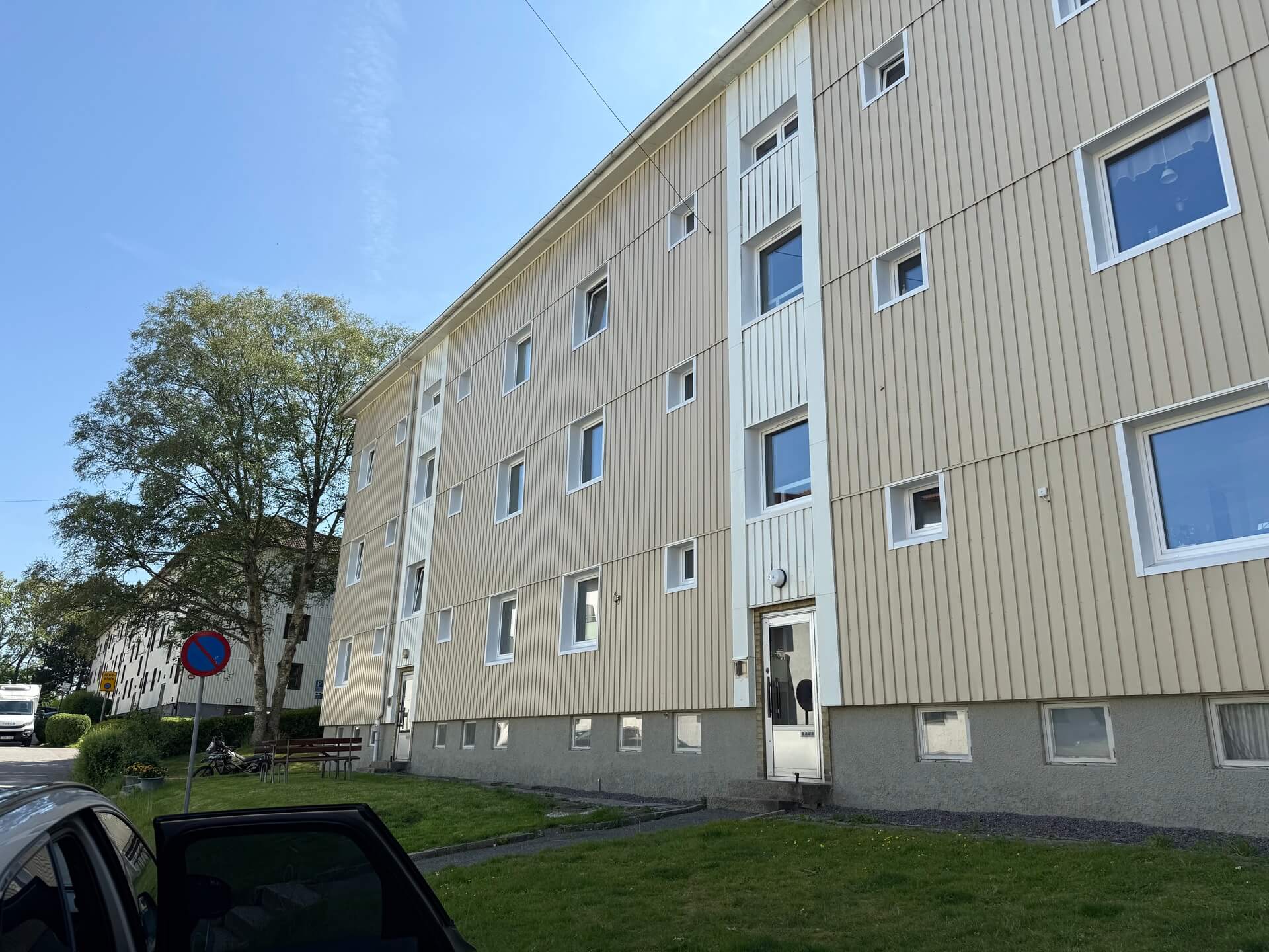 Flerbostadshus med vertikal träpanelfasad och nya vita fönster i solsken