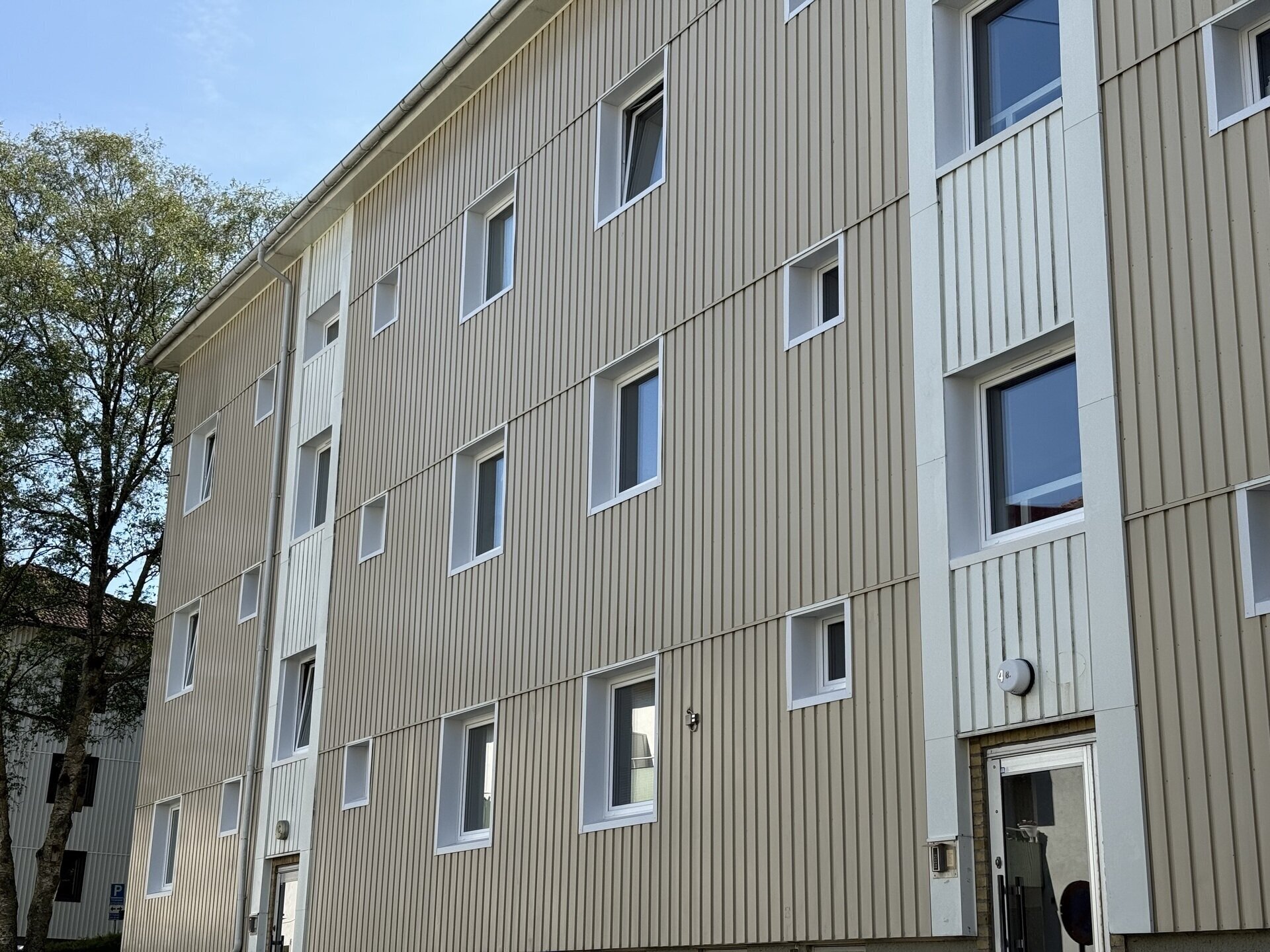 Ljusbeige flerbostadshus med nyinstallerade vita fönster sett från gaveln