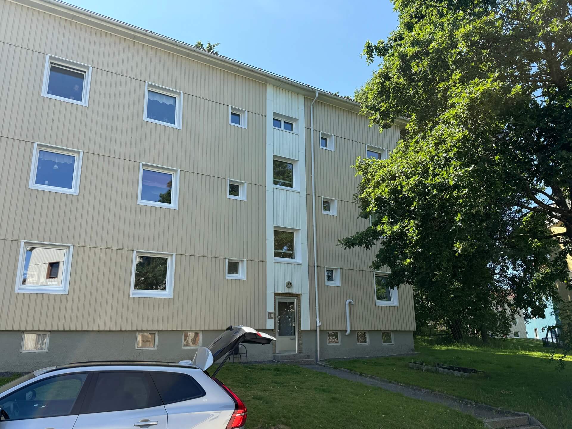 Flerbostadshus med nyinstallerade vita fönster omgärdat av lövträd i sommar