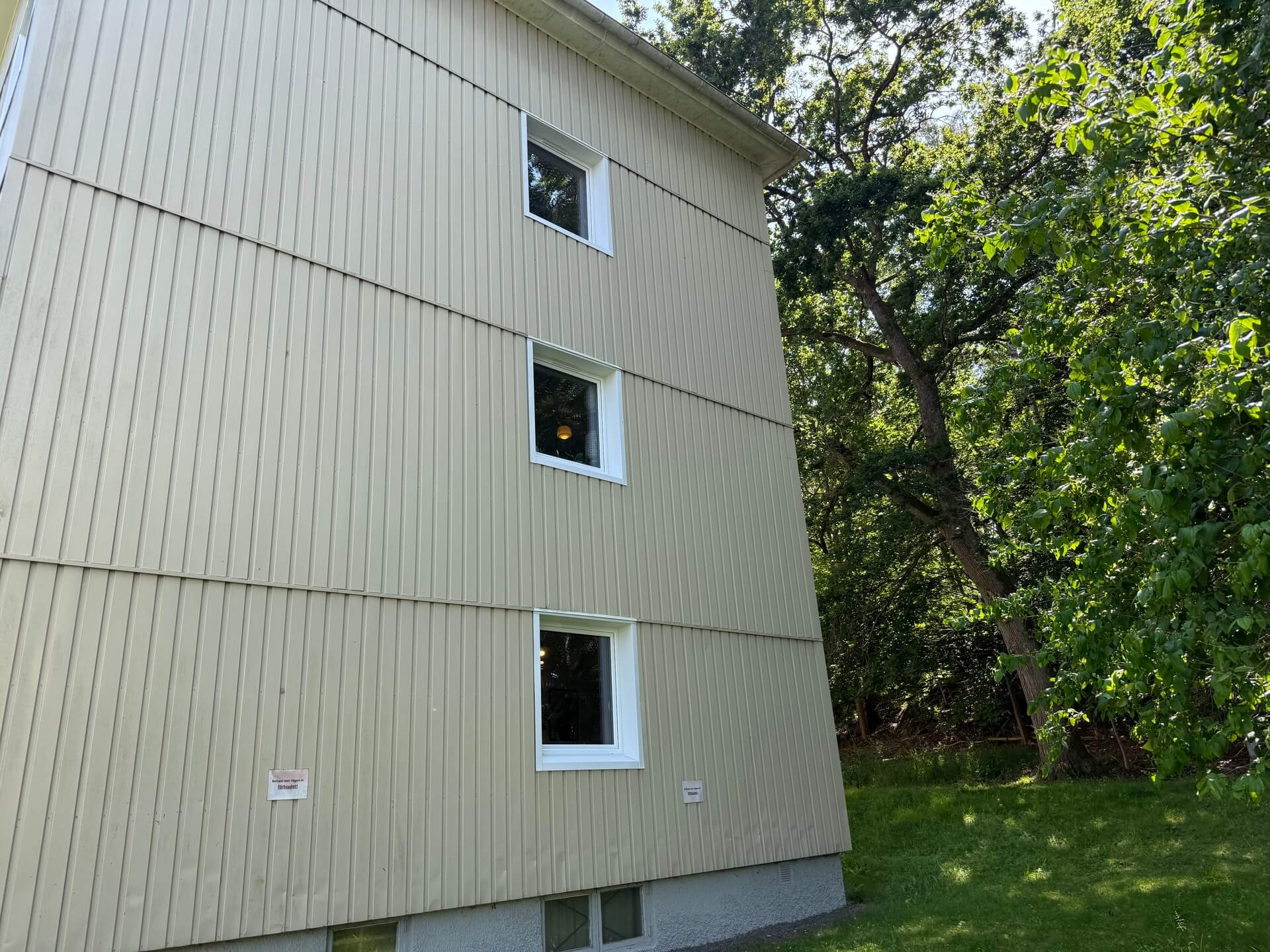 Gavel på flerbostadshus med nyinstallerade vita fönster omgivet av lövträd