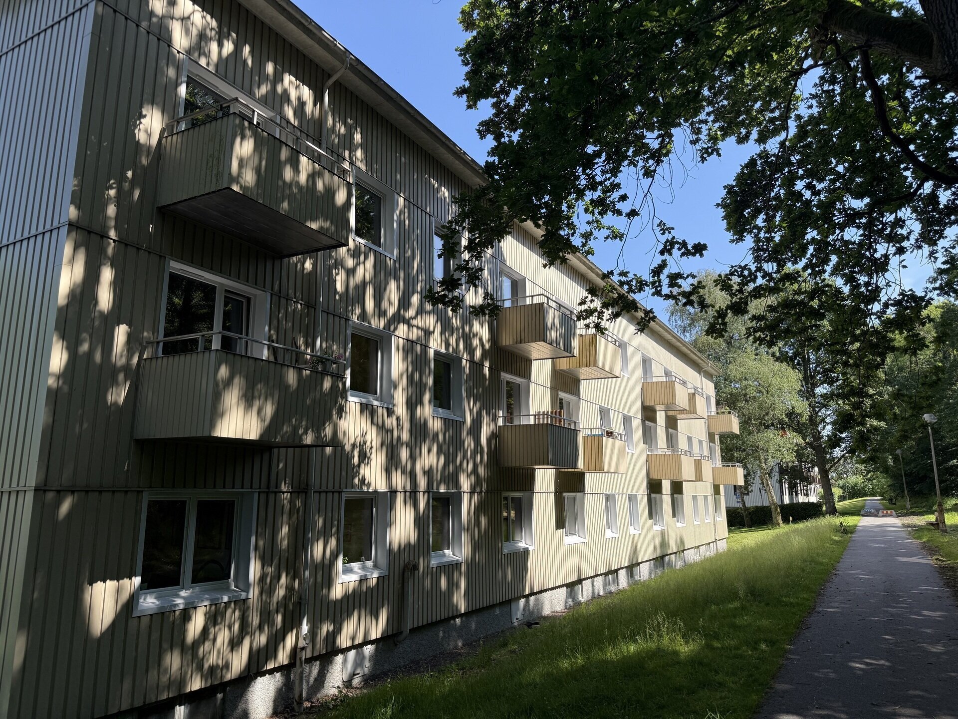Lång rad av flerbostadshus med balkonger och nyinstallerade fönster längs gångväg