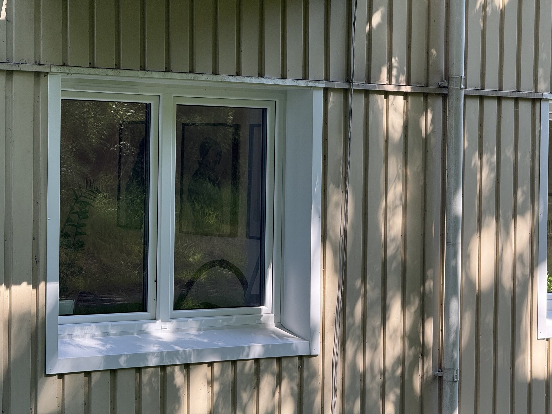 Närbild på nyinstallerat tvåluftsfönster med vit karm och underbleck på träpanelfasad