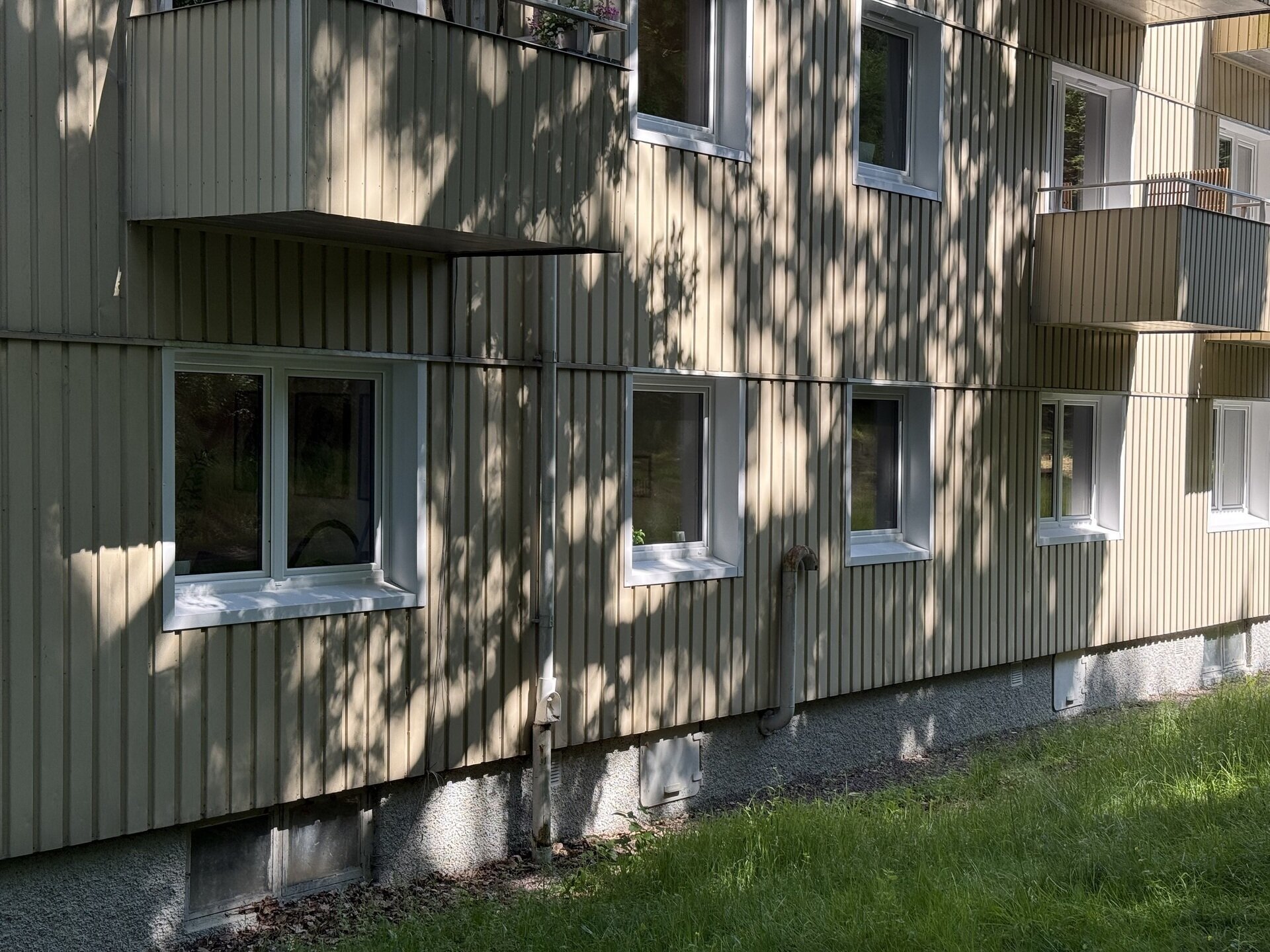 Flerbostadshus med nyinstallerade vita fönster och underbleck på ljus träpanelfasad