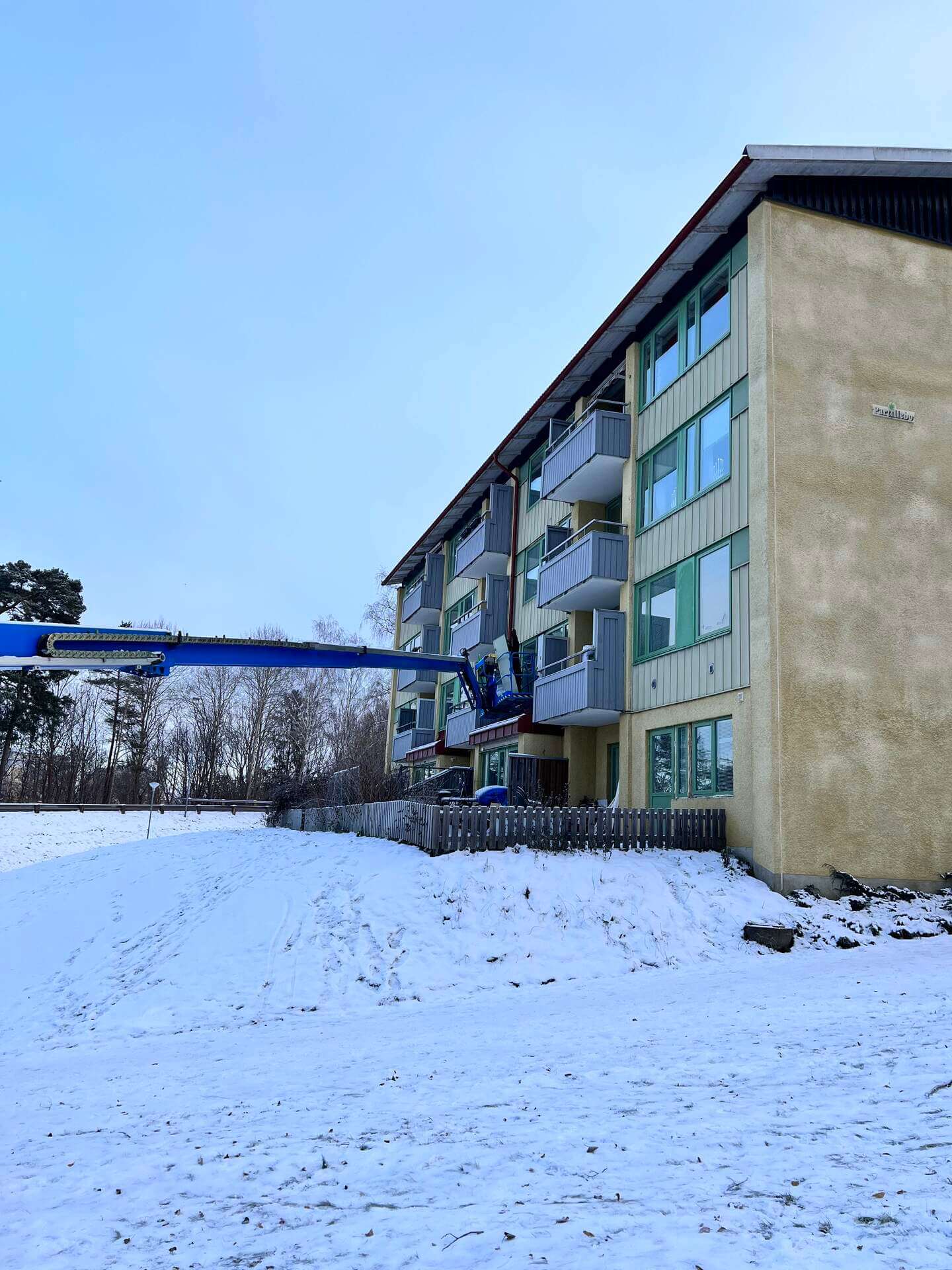 Skylift i arbetsläge vid fasad på flerbostadshus under fönsterbyte i snö